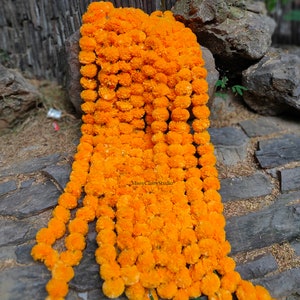 May include: A long garland of bright orange marigold flower blossoms strung together. The garland is lying on a stone surface.