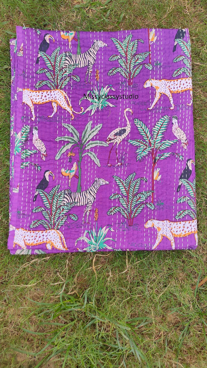 K&ouml;nnte beinhalten: Lilafarbener Kantha-Steppdecke mit einem schwarz-wei&szlig;en Zebra, Tukanen, Flamingos, Leoparden und Palmen. Die Steppdecke hat ein wei&szlig;es Steppmuster.