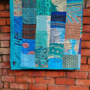 Könnte beinhalten: Eine Patchwork-Decke aus verschiedenen blauen und braunen Stoffen mit unterschiedlichen Mustern. Die Decke hängt an einer Backsteinwand. Die Decke besteht aus vielen verschiedenen Stoffstücken, die zusammengenäht wurden.