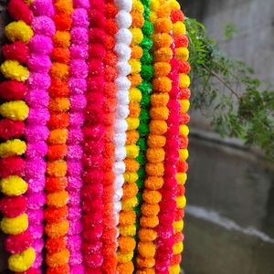 Könnte beinhalten: Eine lebendige Girlande aus bunten Pompons in Rosa, Orange, Gelb, Weiß und Grün. Die Pompons sind in vertikalen Reihen angeordnet und erzeugen eine festliche und auffällige Darstellung. Die Girlande wird wahrscheinlich zur Dekoration verwendet.