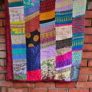 Könnte beinhalten: Eine farbenfrohe Patchwork-Decke aus wiederverwendeten Stoffresten. Die Decke besteht aus verschiedenen geometrischen Formen und Mustern in Blautönen, Grün, Rot, Lila und Gelb. Die Decke ist handgenäht und hat einen einzigartigen, rustikalen Look.