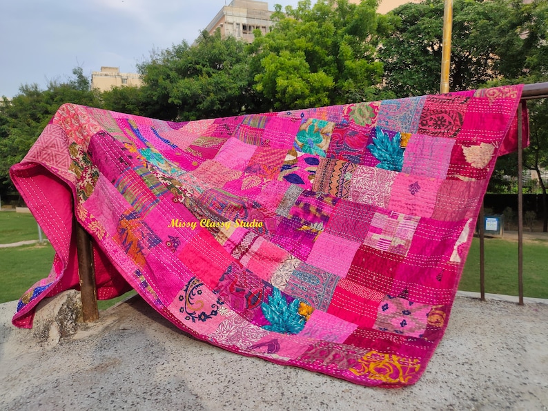 Peut inclure: Une courtepointe rose vif avec un patchwork de motifs et de textures vari&eacute;s. La courtepointe est drap&eacute;e sur une barre m&eacute;tallique, mettant en valeur son design complexe et ses variations de couleurs. Le texte "Missy Class Studio" est visible.