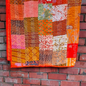 May include: A patchwork quilt with a variety of colors and patterns, including orange, red, brown, and white. The quilt is made of different fabrics sewn together in a random pattern.