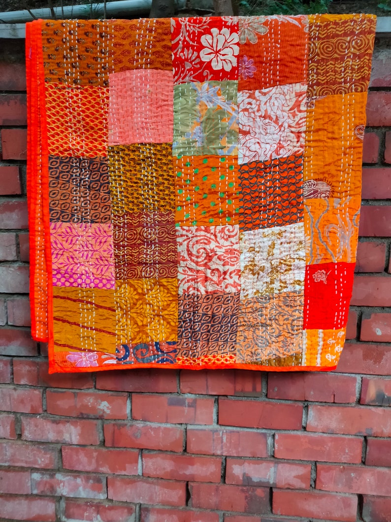 May include: A patchwork quilt with a variety of colors and patterns, including orange, red, brown, and white. The quilt is made of different fabrics sewn together in a random pattern.