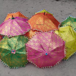 Könnte beinhalten: Eine Sammlung bunter, dekorativer Regenschirme. Die Regenschirme sind in Pink-, Orange-, Grün- und Gelbtönen gehalten und mit goldenen Blumenmustern versehen. Jeder Regenschirm hat eine dekorative Bordüre an den Rändern.