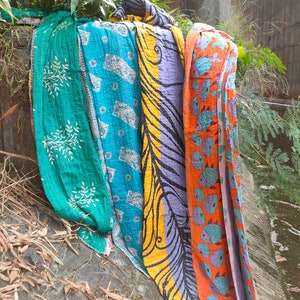 May include: Four colorful kantha quilts with different patterns, including a teal quilt with white floral designs, a blue quilt with white geometric designs, a yellow and purple quilt with black swirls, and an orange quilt with blue fish designs.