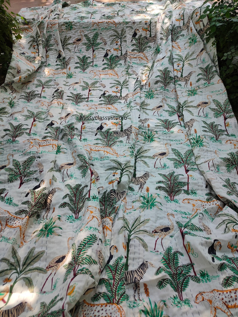 K&ouml;nnte beinhalten: Wei&szlig;e Baumwolldecke mit einem sich wiederholenden Muster aus gr&uuml;nen Palmen, Zebras, Leoparden, Flamingos und Tukanen. Die Decke ist in der H&auml;lfte gefaltet und hat eine subtile gesteppte Textur.