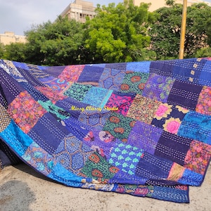Peut inclure: Une courtepointe patchwork aux tons bleus vari&eacute;s, du bleu marine au bleu ciel clair. La courtepointe pr&eacute;sente un m&eacute;lange de motifs floraux et g&eacute;om&eacute;triques, avec des coutures visibles. La courtepointe est drap&eacute;e sur un support, mettant en valeur sa texture et son design.