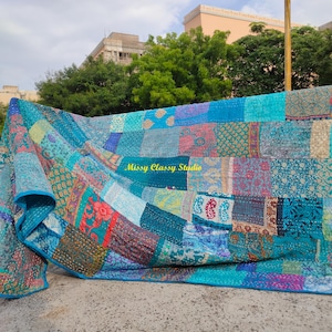 Peut inclure: Une courtepointe patchwork dans les tons de bleu, sarcelle et turquoise, avec une vari&eacute;t&eacute; de carr&eacute;s de tissu &agrave; motifs. La courtepointe est drap&eacute;e sur une rampe, mettant en valeur son design et ses textures complexes. Le texte "Missy Classy Studio" est visible.