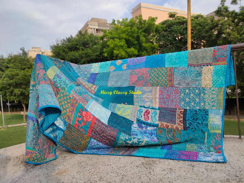Peut inclure: Une courtepointe patchwork dans les tons de bleu, sarcelle et turquoise, avec une vari&eacute;t&eacute; de carr&eacute;s de tissu &agrave; motifs. La courtepointe est drap&eacute;e sur une rampe, mettant en valeur son design et ses textures complexes. Le texte "Missy Classy Studio" est visible.