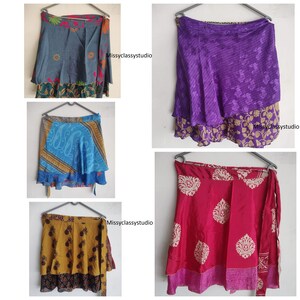 Könnte beinhalten: Sammlung von Wickelröcken in verschiedenen Farben und Mustern. Die Röcke werden auf Kleiderbügeln vor weißem Hintergrund präsentiert. Designs umfassen Blumen-, Paisley- und geometrische Drucke in Blau-, Lila-, Gelb- und Rottönen. Die Röcke sind aus leichtem Stoff.