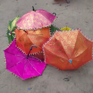 May include: A group of five colorful umbrellas with gold accents and fringed edges. The umbrellas are made of a patterned fabric and have wooden handles.