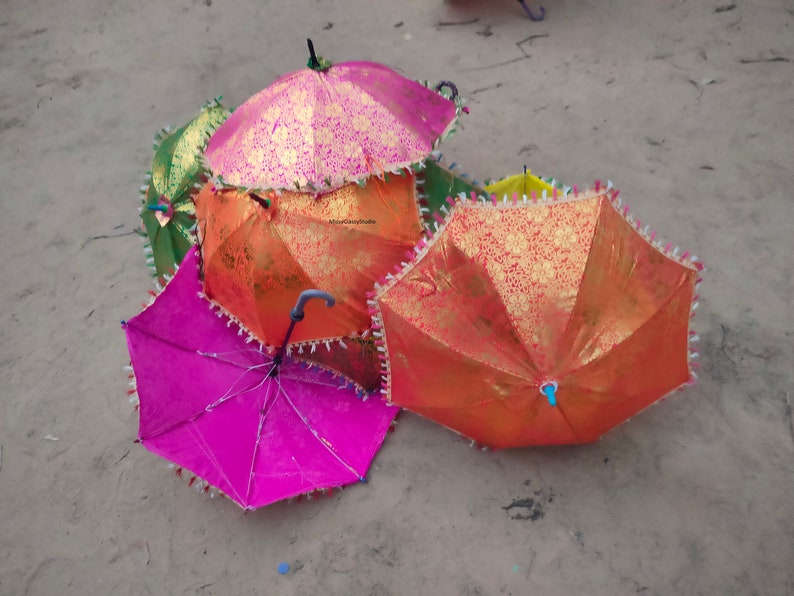 May include: A group of five colorful umbrellas with gold accents and fringed edges. The umbrellas are made of a patterned fabric and have wooden handles.