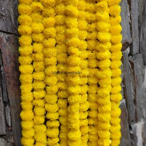 Könnte beinhalten: Eine Girlande aus leuchtend gelben Ringelblumenblüten, die aneinandergereiht sind. Die Girlande hängt an einer Steinmauer.