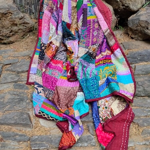 Może przedstawiać: Patchworkowa kołdra z żywą mieszanką kolorów i wzorów. Kołdra posiada różnorodne tkaniny w odcieniach różu, fioletu, niebieskiego i zielonego. Krawędzie obszyte są ciemnoczerwoną tkaniną. Wymiary w centymetrach.