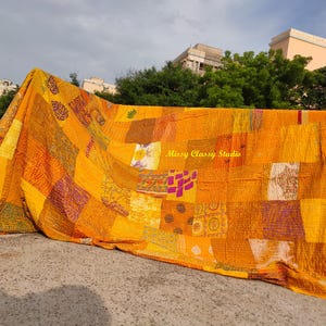 Peut inclure: Une courtepointe patchwork vibrante dans les tons de jaune, orange et violet. La courtepointe est compos&eacute;e de divers carr&eacute;s de tissu avec diff&eacute;rents motifs et textures. La courtepointe est drap&eacute;e sur une rampe, avec le texte "Missy Classy Studio" visible.