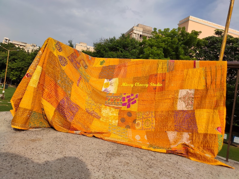 Peut inclure: Une courtepointe patchwork vibrante dans les tons de jaune, orange et violet. La courtepointe est compos&eacute;e de divers carr&eacute;s de tissu avec diff&eacute;rents motifs et textures. La courtepointe est drap&eacute;e sur une rampe, avec le texte "Missy Classy Studio" visible.