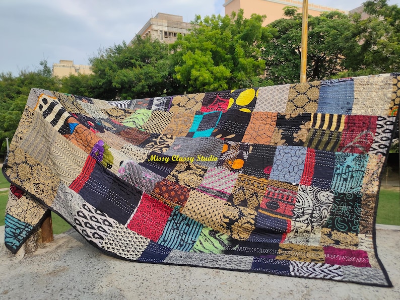 Peut inclure: Une courtepointe patchwork avec une vari&eacute;t&eacute; de carr&eacute;s de tissu &agrave; motifs dans des tons de noir, bleu, rouge et or. La courtepointe est drap&eacute;e sur une surface, mettant en valeur son design et ses textures complexes. Le texte "Missy Classy Studio" est visible.