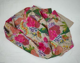 May include: A beige textile with a vibrant floral pattern. The design features large pink flowers, green leaves, and orange and yellow accents. The fabric is folded, showcasing the intricate stitching and design.
