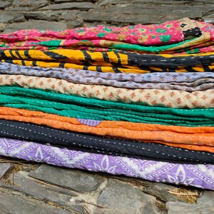 May include: A stack of colorful kantha quilts with various patterns and stitching. The quilts are made of recycled saris and are a traditional Indian craft.
