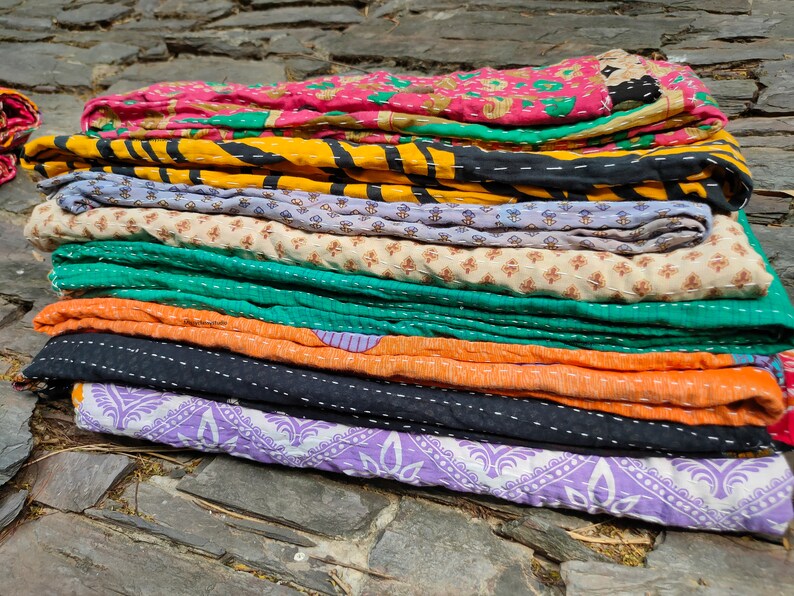 May include: A stack of colorful kantha quilts with various patterns and stitching. The quilts are made of recycled saris and are a traditional Indian craft.