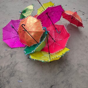May include: A group of colorful umbrellas with fringe trim. The umbrellas are in various shades of pink, red, yellow, green, and orange. The umbrellas are lying on a sandy surface.