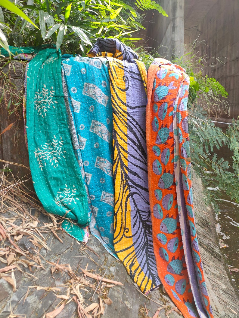 Puede incluir: Cuatro colchas kantha coloridas con varios patrones, incluyendo dise&ntilde;os florales, paisley y de peces. Las colchas est&aacute;n hechas de algod&oacute;n y est&aacute;n cosidas a mano. Est&aacute;n drapeadas sobre una pared de piedra y cuelgan parcialmente.