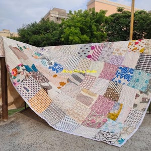 Peut inclure: Une courtepointe patchwork avec une vari&eacute;t&eacute; de motifs et de couleurs, notamment des motifs floraux, g&eacute;om&eacute;triques et abstraits. La courtepointe est compos&eacute;e de carr&eacute;s de tissu de diff&eacute;rentes couleurs, notamment rose, bleu, blanc et marron. La courtepointe est drap&eacute;e sur une structure m&eacute;tallique.