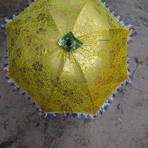 May include: A yellow umbrella with a floral pattern and a black handle. The umbrella has a fringe trim with blue, white, and green accents.