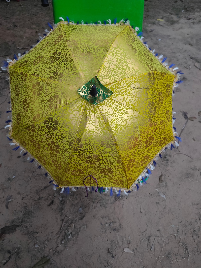 May include: A yellow umbrella with a floral pattern and a black handle. The umbrella has a fringe trim with blue, white, and green accents.
