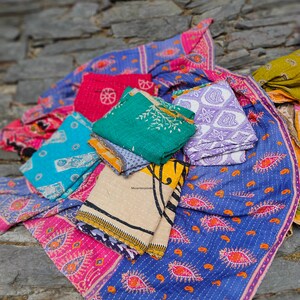 May include: A stack of colorful kantha quilts with various patterns, including paisley, floral, and geometric designs. The quilts are made of recycled saris and are perfect for adding a touch of bohemian style to any home.