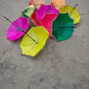 May include: A group of colorful umbrellas with fringed edges. The umbrellas are in various shades of pink, green, yellow, and orange. The umbrellas are arranged in a circle on a sandy surface.