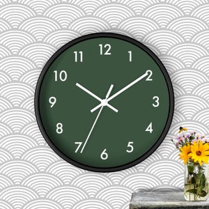 May include: A round, black framed clock with white numbers and hands. The clock face is a dark green color. The clock is hanging on a white and gray patterned wall.
