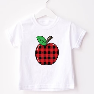 May include: White t-shirt with a red and black plaid apple graphic.