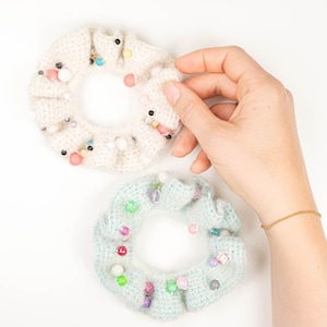 May include: Two crocheted hair scrunchies with colourful beads. The scrunchies are white and light blue.