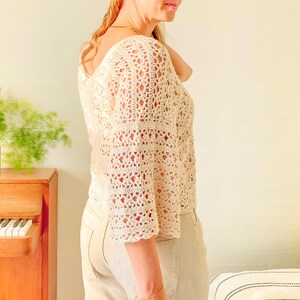 May include: A white crochet top with a loose, flowy fit and a square neckline. The top has a delicate, lacy pattern and is perfect for a summer day.