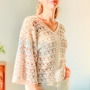 May include: A white crochet top with a v-neck and bell sleeves. The top is made with a delicate open stitch pattern.
