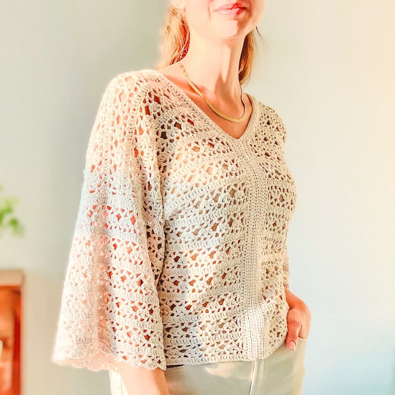 May include: A white crochet top with a v-neck and bell sleeves. The top is made with a delicate open stitch pattern.