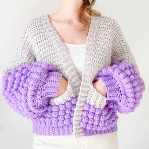 May include: A crocheted cardigan with a grey body and purple sleeves. The sleeves have a textured, puffy design.