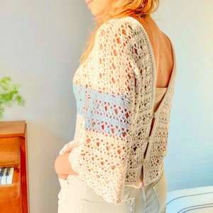 May include: A white crochet top with a blue and white striped detail. The top has a loose fit and a deep V-neckline.