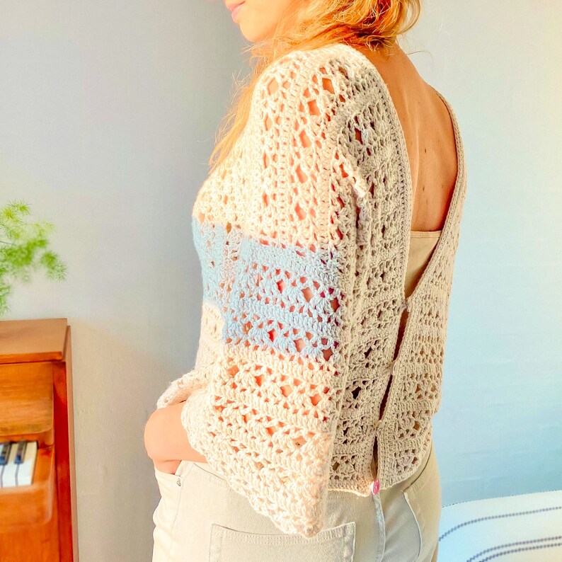 May include: A white crochet top with a blue and white striped detail. The top has a loose fit and a deep V-neckline.