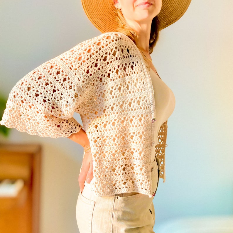 May include: A crocheted cardigan with a delicate openwork pattern in a cream color. The cardigan has a relaxed fit and three-quarter sleeves.