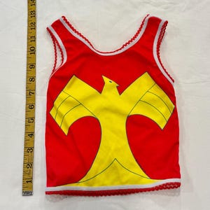 May include: A red tank top with a yellow bird design. The tank top has white trim and a decorative red and white trim along the edges. The tank top is approximately 10 inches long.