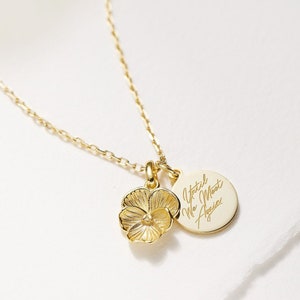 May include: Gold necklace with a delicate chain and two charms. One charm is a small, detailed flower, and the other is a round disc with the inscription "Until We Meet Again".