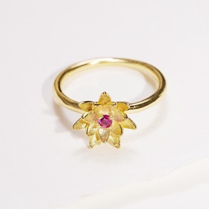 以下が含まれることがあります： 中央にピンクの宝石がセットされた、5枚の花びらを持つ花の形をした金のリングです。