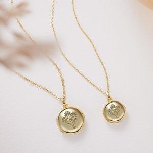 May include: Two gold necklaces with delicate chains and round lockets. Each locket features a floral design.