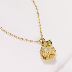 May include: A gold chain necklace with a delicate flower pendant featuring a small green gemstone accent.