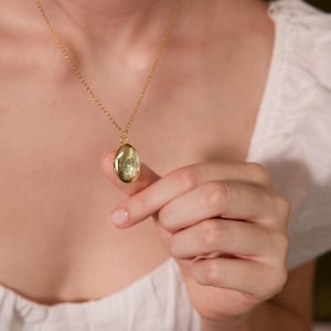 Puede incluir: Un collar de cadena de oro con un colgante de medall&oacute;n ovalado de oro con un dise&ntilde;o floral.