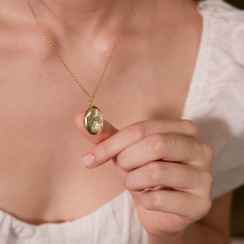 Puede incluir: Un collar de cadena de oro con un colgante de medall&oacute;n ovalado de oro con un dise&ntilde;o floral.