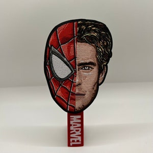 May include: A red and black embroidered patch of Spider-Man's face with the right side of his face showing Tom Holland's face. The patch is attached to a red backing with the word "MARVEL" in white lettering.